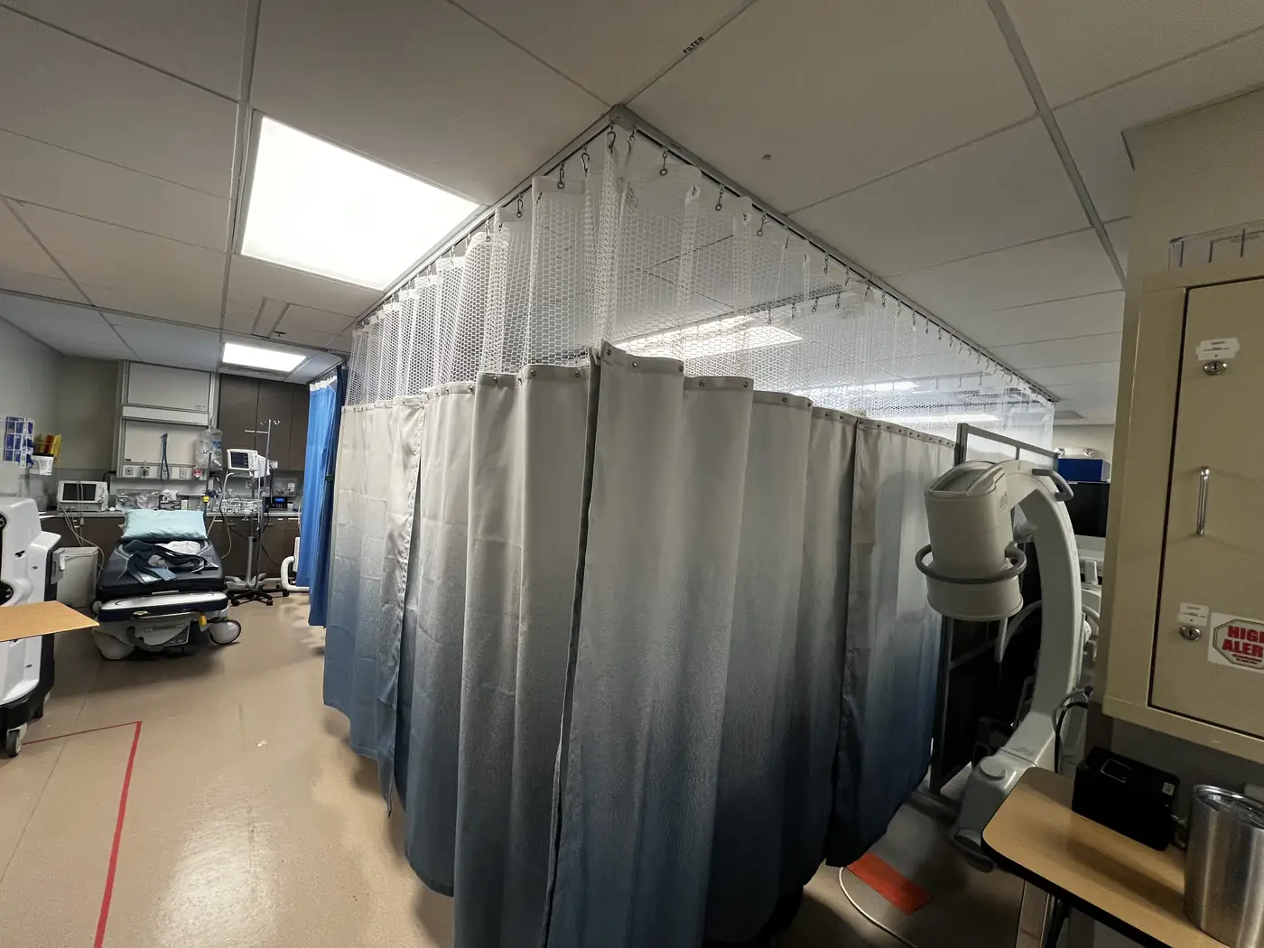 Cubicle curtains on ceiling track enclosing pre-operative bays in a San Francisco surgery center, mesh tops left open to the sprinklers