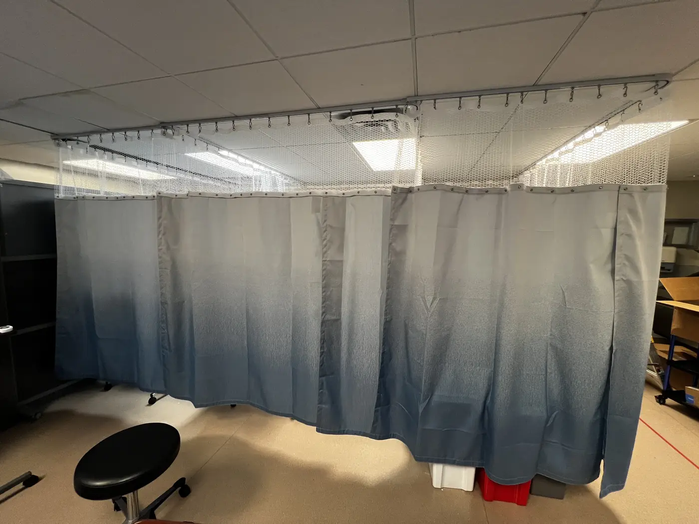 A continuous ceiling curtain track turning a curved corner in a San Francisco clinical area, carriers loaded and the mesh top hung