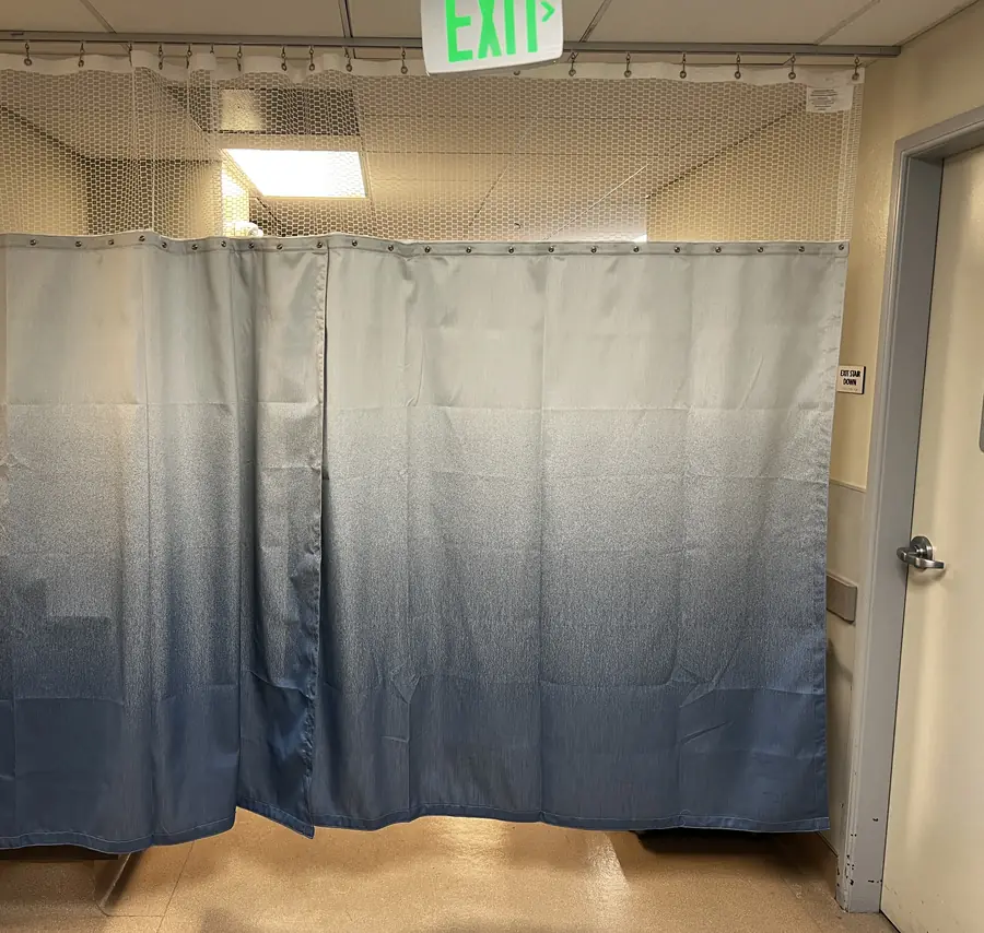 A hospital privacy curtain with a grommet header and mesh top hung on corridor track in a San Francisco surgery center